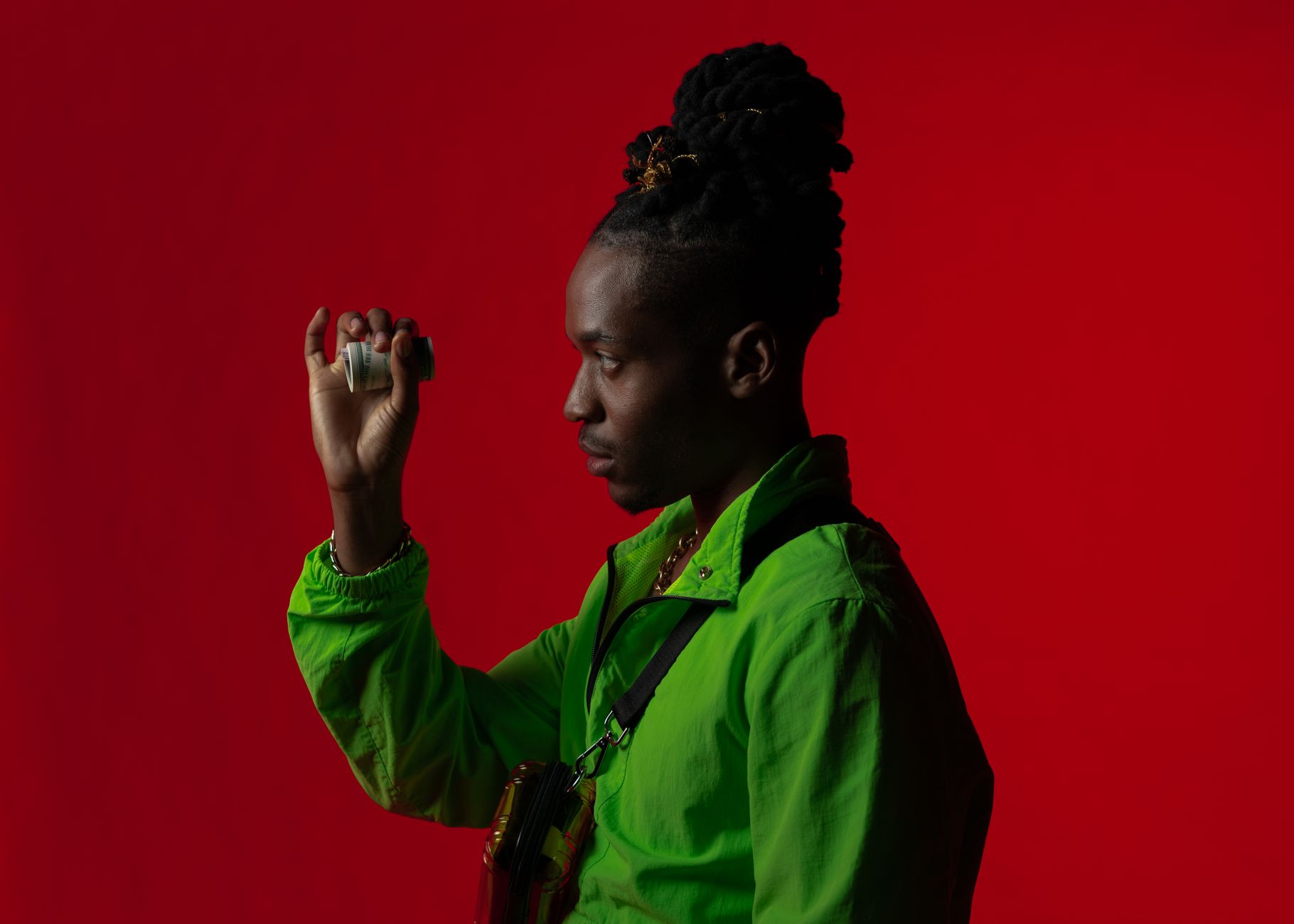 Fashionable African American man with dreadlocks holding money against a red backdrop.