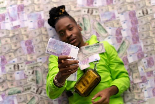 Free Confident man in green jacket holding a 500 euro note amidst a sea of currency Stock Photo