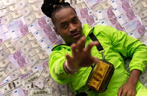 Free Man lying on a pile of cash, wearing a bright green jacket, symbolizes wealth and success. Stock Photo