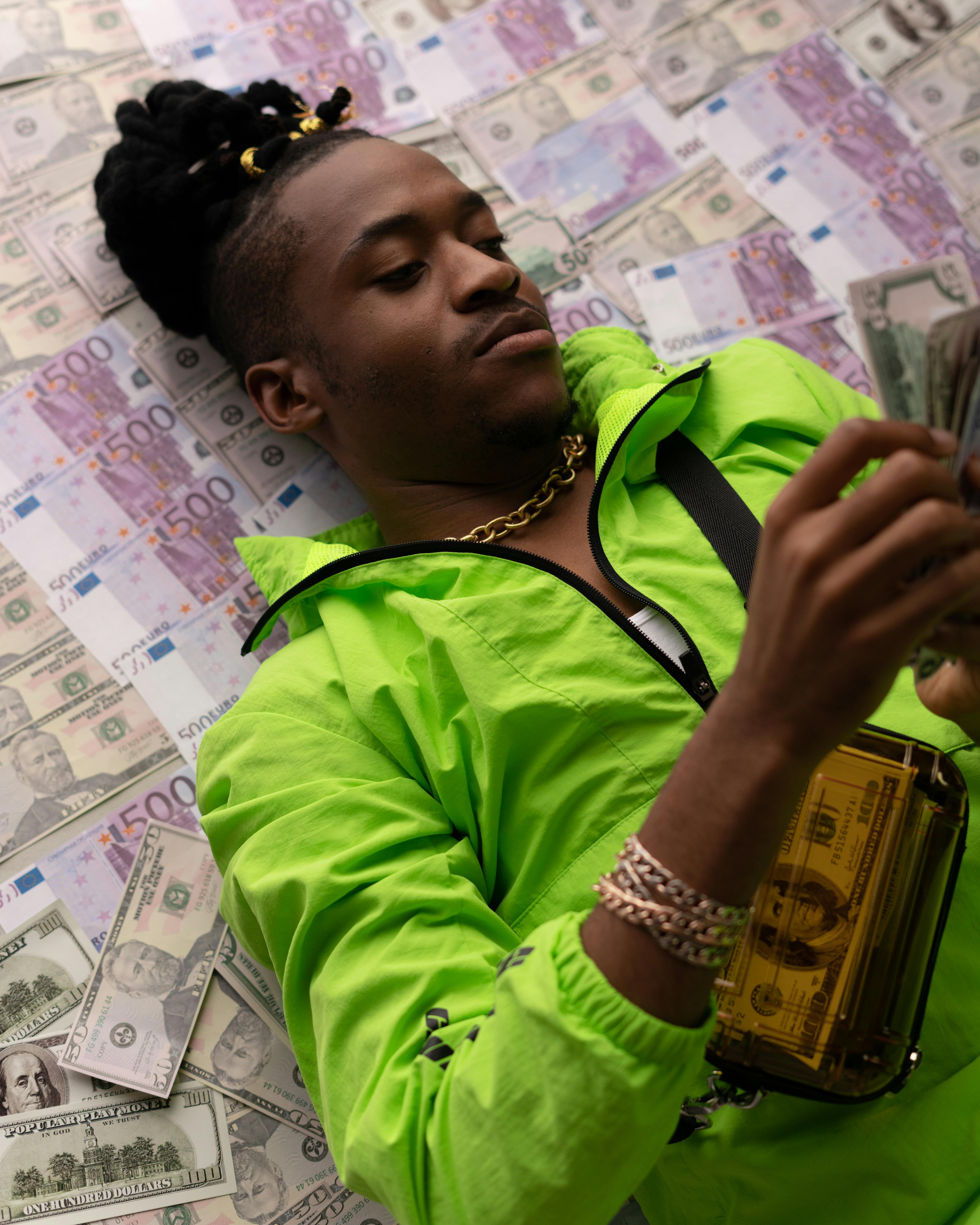 man in green jacket lying down on money