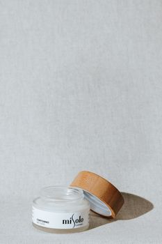 Elegant open cosmetic jar with wooden lid on a textured white backdrop.