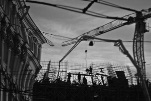 From below black and white of builders on construction site near tall crane and building