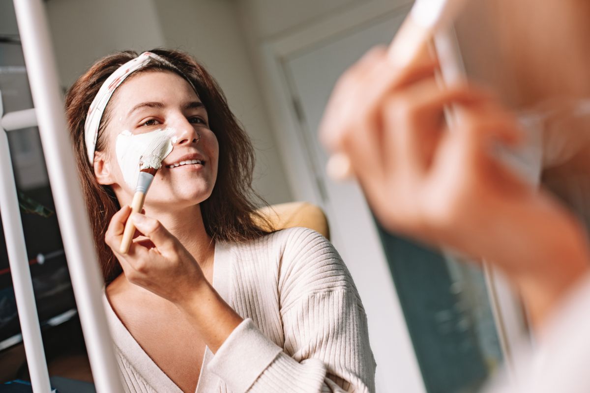 Woman applying a herbal face mask in front of a mirror as part of her beauty ritual