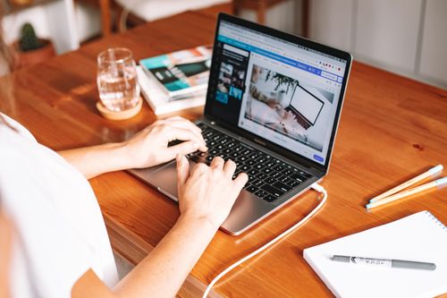 Free A person working remotely on a laptop at a wooden desk with stationery and a notepad. Stock Photo