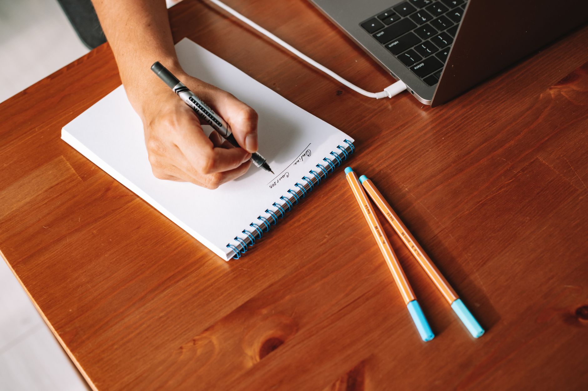 A hand writing short notes in a notebook beside a laptop, the two lines written straight after a session
