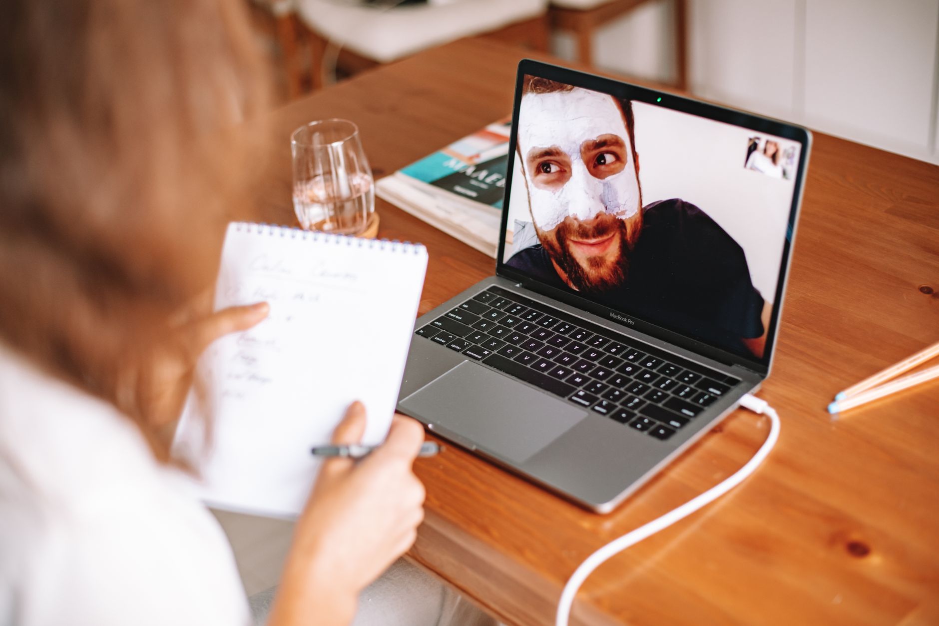 A coach at a home desk with a notebook, talking with a client on a laptop video call