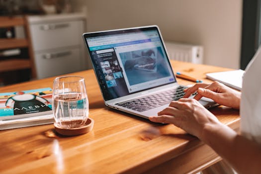 Close-up of hands on a laptop in a cozy home office with a water glass on desk.