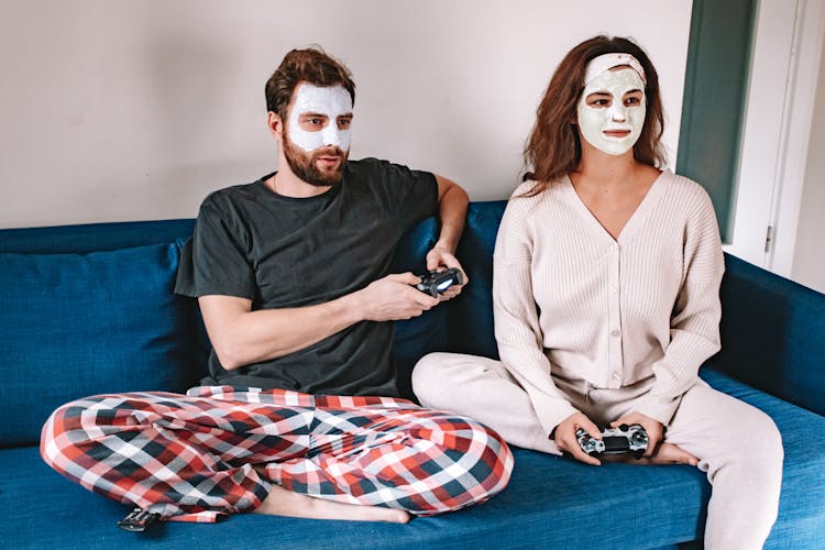 Man And Woman With Facial Cream Sitting On Couch Playing Video Game