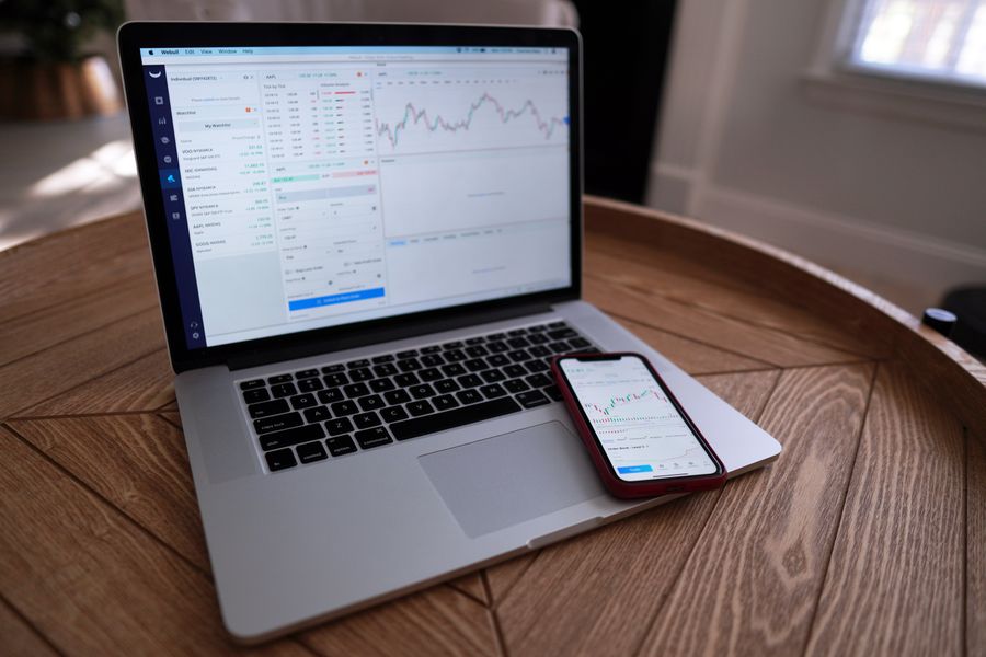 Laptop and smartphone showing financial graphs on a wooden table indoors.