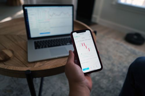 Free Person using smartphone with stock market charts while laptop displays data. Indoor setting. Stock Photo
