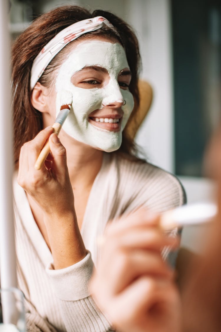 Woman Holding A Brush Applying Facial Cream On Face