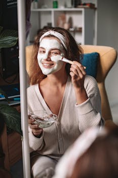 Smiling woman applying a clay face mask at home, enjoying a relaxing skincare routine.