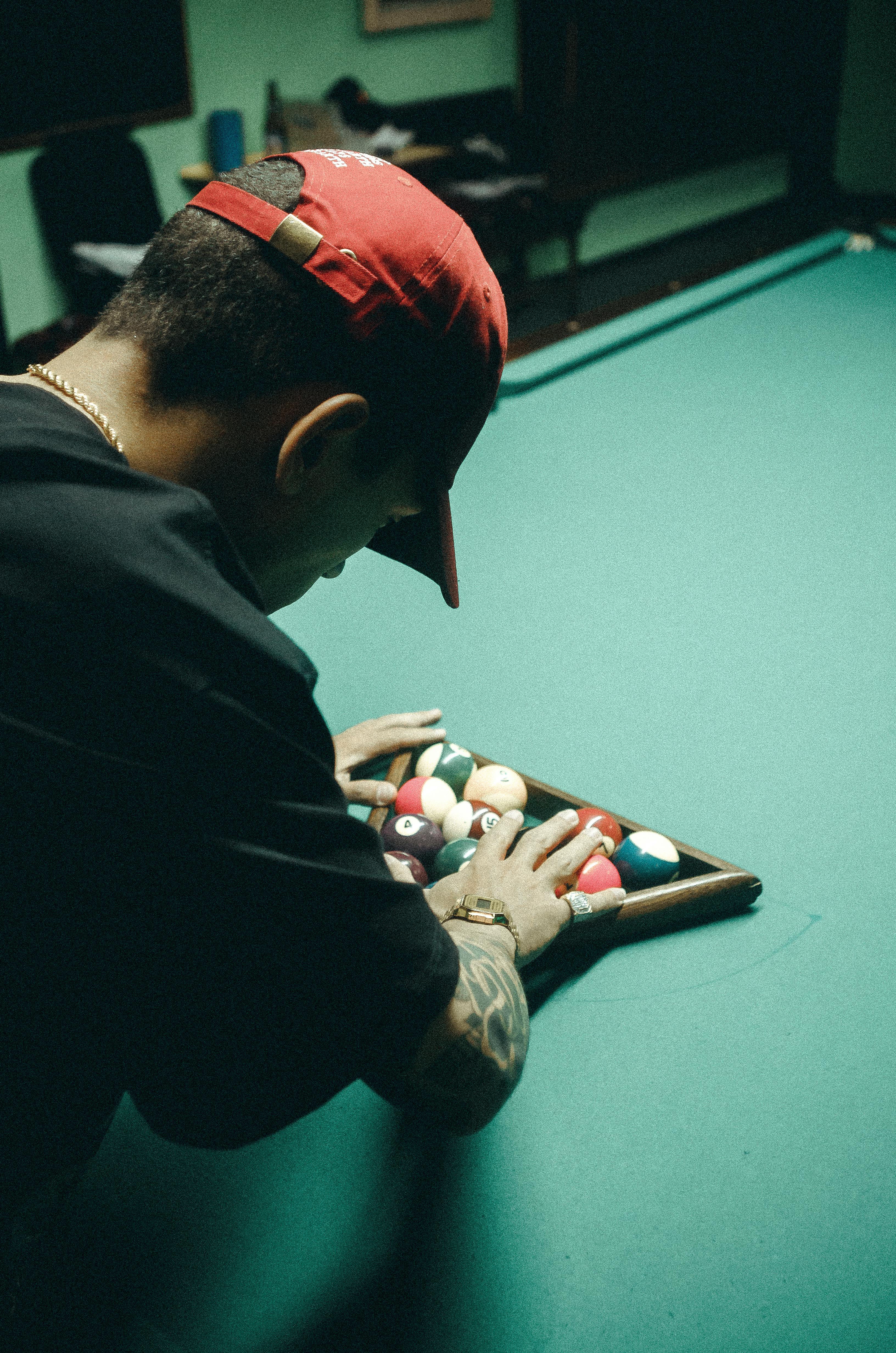 Man in Black Tshirt and Red Baseball Cap Arranging Billiard Balls on