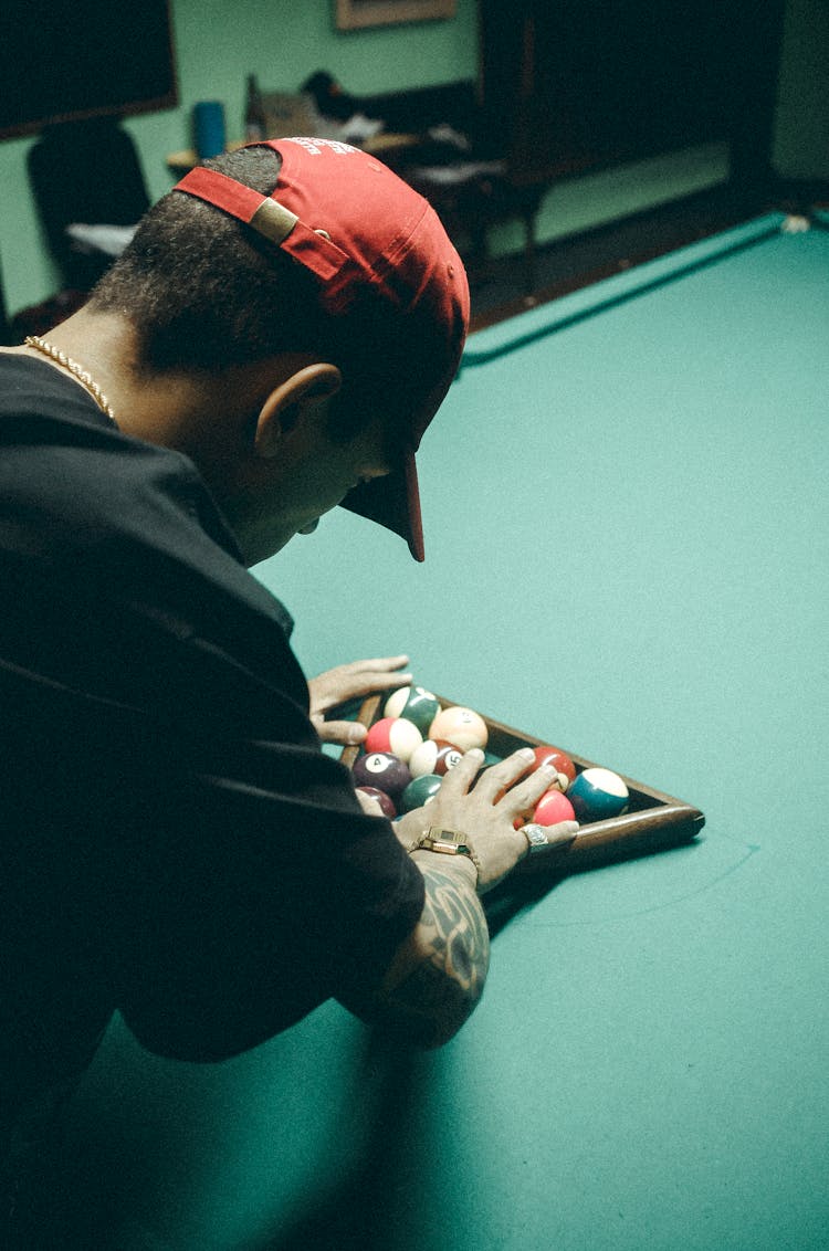 Man In Black T-shirt And Red Baseball Cap Arranging Billiard Balls On Table