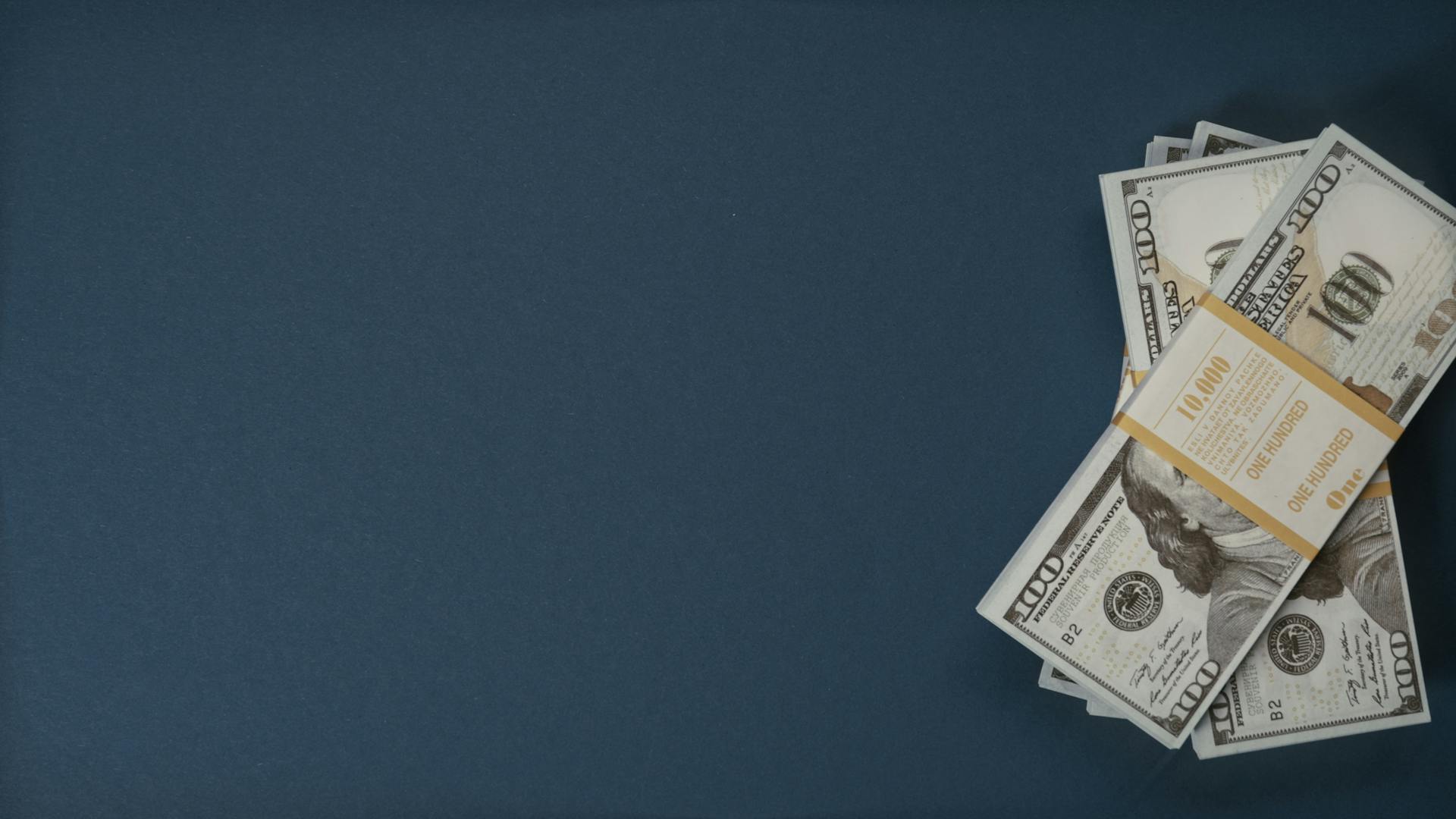 A bundle of US dollar bills on a dark blue background with ample copy space.