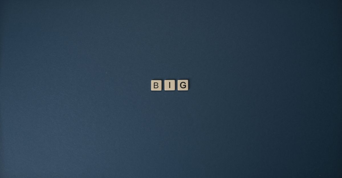 Minimalist image of Scrabble tiles spelling 'BIG' on blue surface.