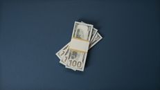 黑色的表面上堆着一叠100美元纸币，象征着财富与金融