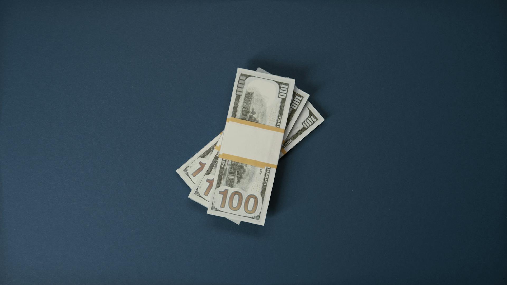 Stack of 100 US dollar bills on a dark surface, symbolizing wealth and finance.