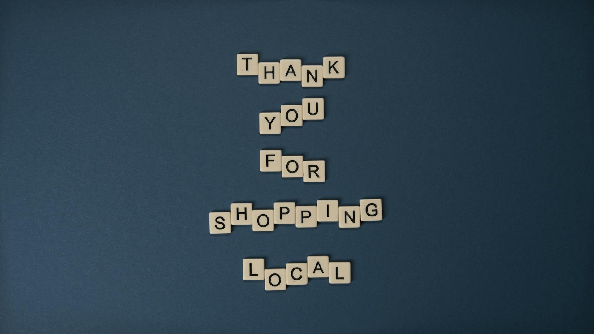 Scrabble-style letter tiles forming message on blue background: Thank you for shopping local.