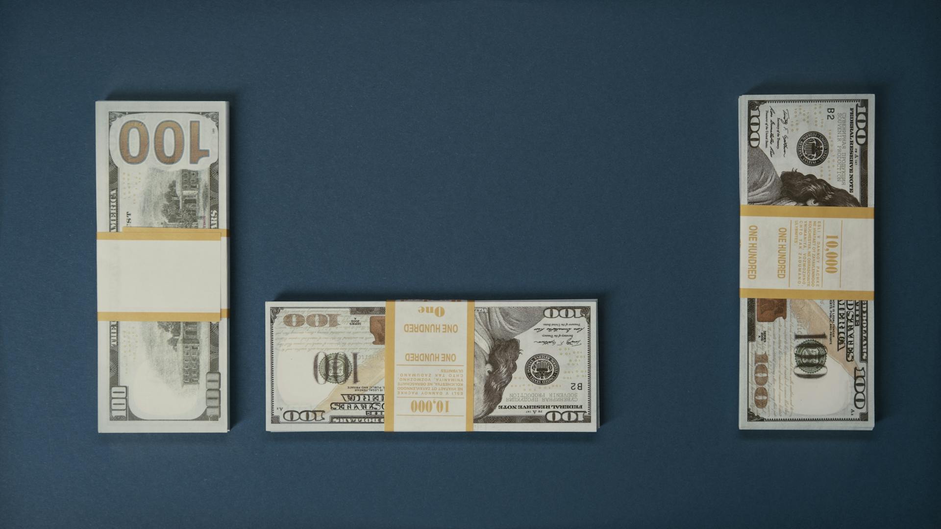 Neatly arranged stacks of 100 US dollar bills on a clean blue background, symbolizing wealth and finance.