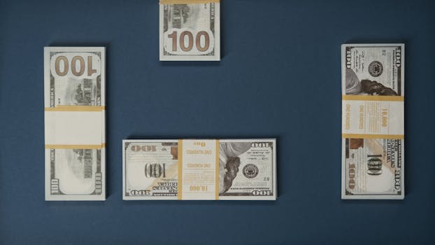 Flat lay of multiple stacks of 100 dollar bills on a blue background, symbolizing wealth and finance.