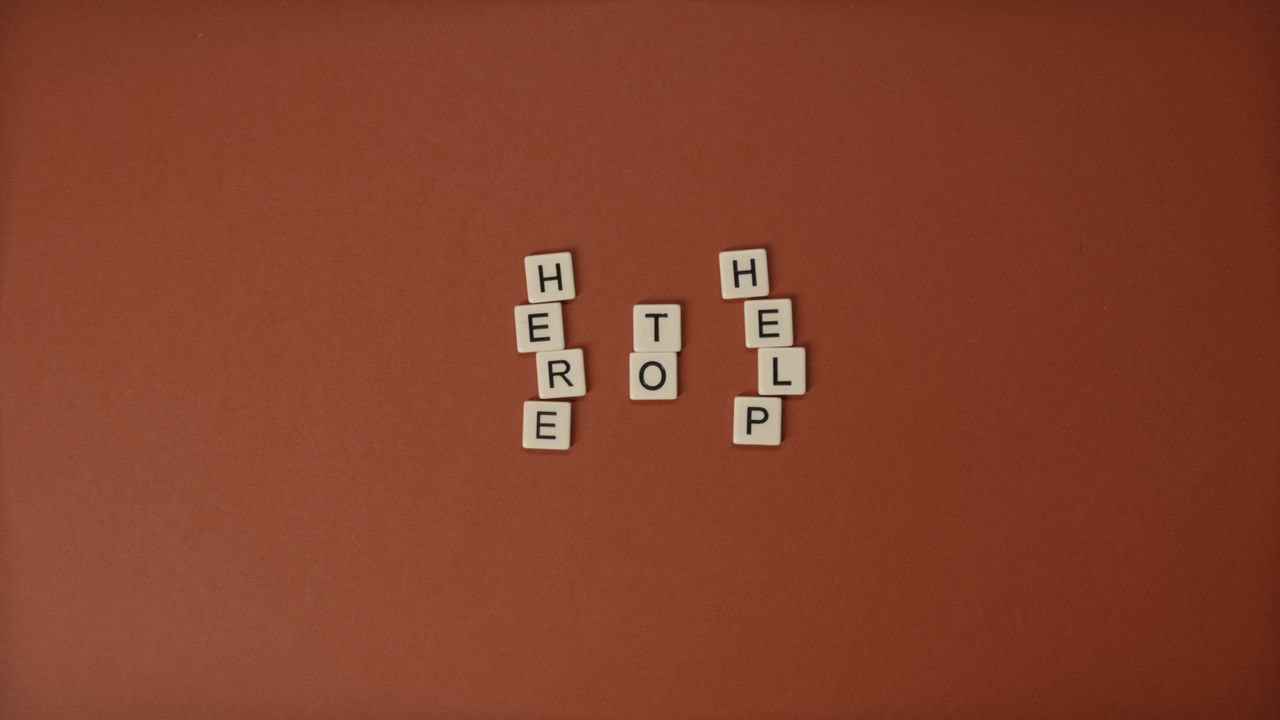 flat lay of scrabble tiles spelling here to help on a brown background