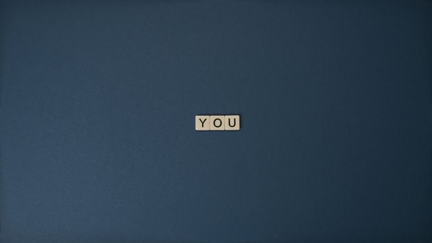 Flat lay of Scrabble letters spelling 'YOU' on a blue background, perfect for conceptual themes.