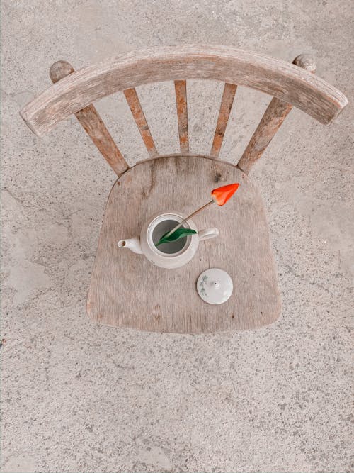 Top view composition of fragrant red tulip in ceramic teapot placed on wooden chair