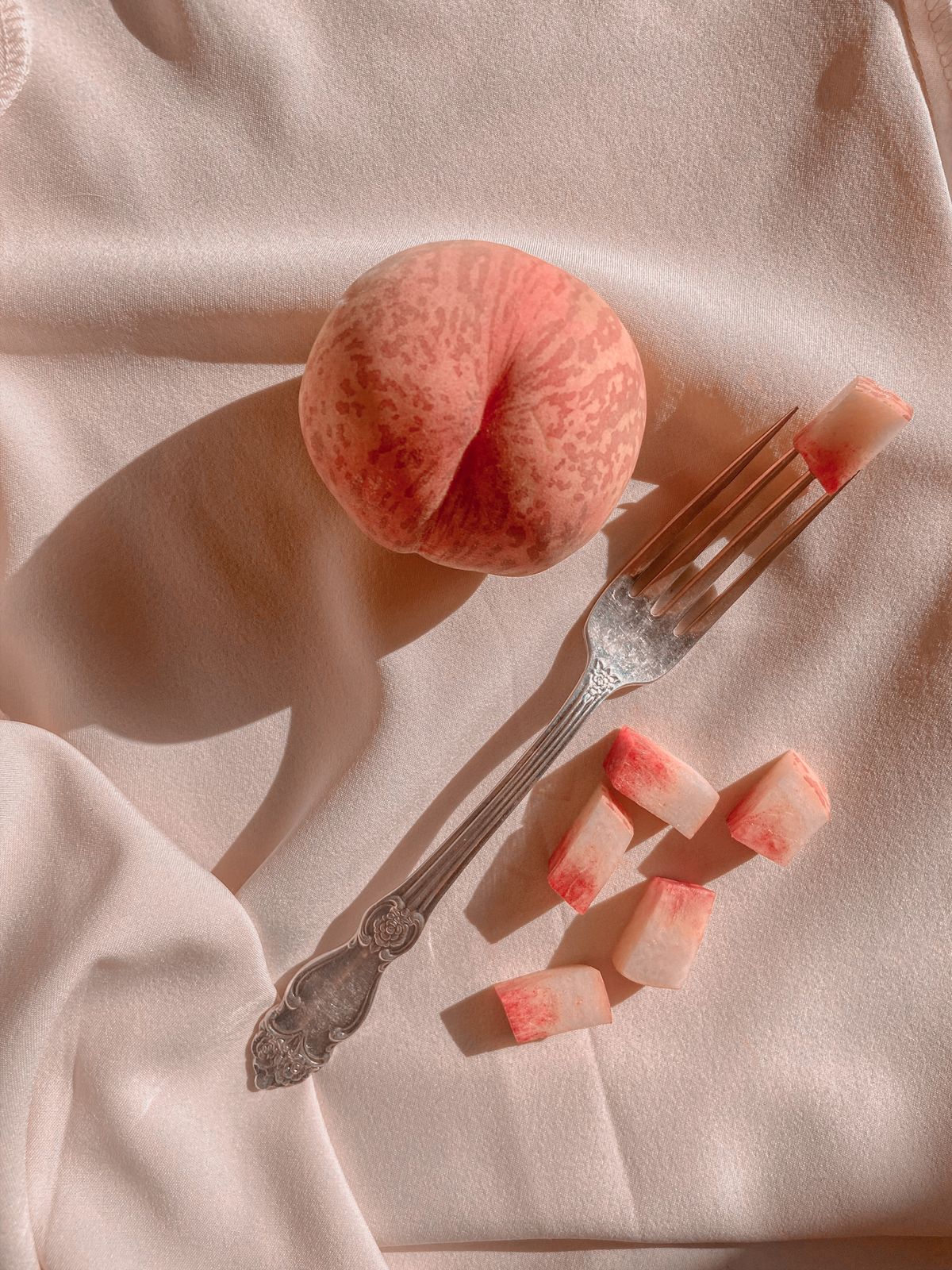 Ripe peach with a fork on draped silk fabric
