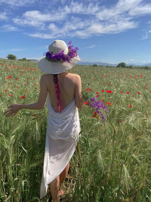 Back view of anonymous female wearing straw hat carrying blooming bouquet of flowers in meadow in summer day