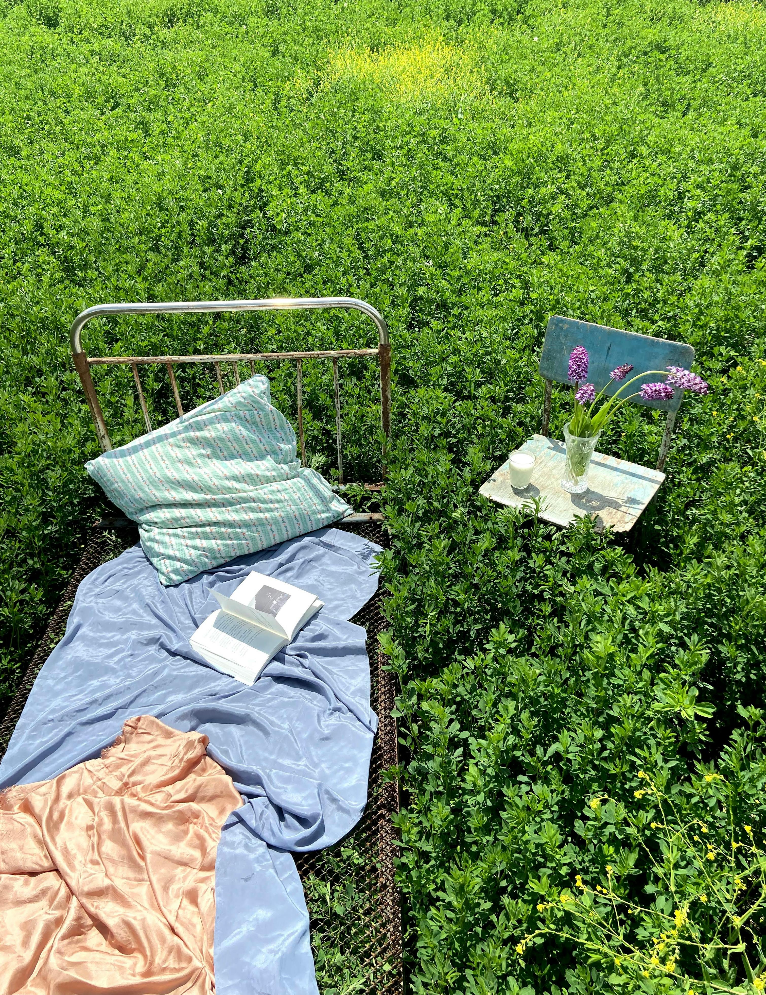 bed with book near chair with flower bunch in field