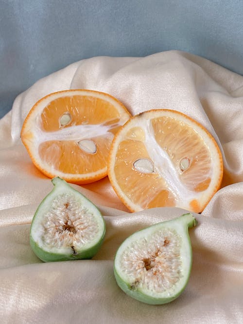 Composition of halves of healthy fresh orange and fig placed on soft silk fabric