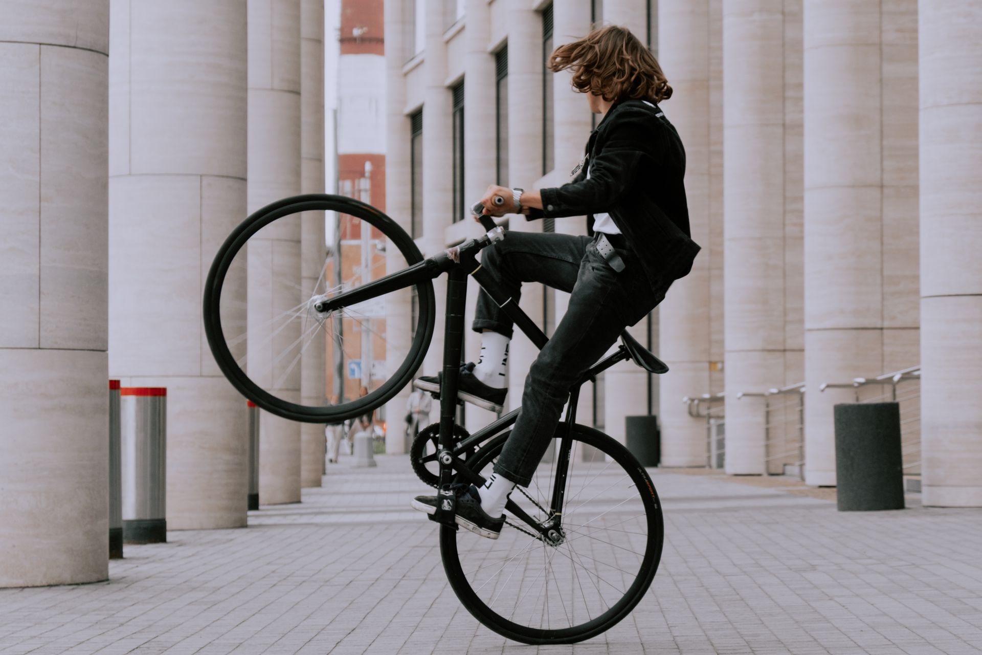 Action shot of a man doing a bicycle wheelie in an urban setting with tall columns.