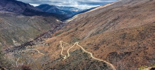 Free Spectacular view of a winding road through a mountainous landscape under a dynamic sky. Stock Photo