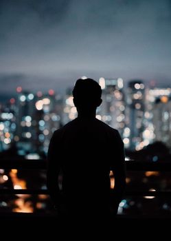 一名男子的剪影出现在阳台上，俯瞰着下方夜晚充满活力、灯光闪闪发光的城市景观