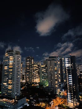 Vibrant urban skyline showcasing illuminated skyscrapers under a dramatic night sky.