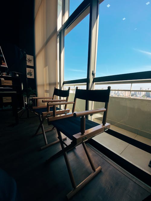 Interior of stylish room with wooden armchairs placed near panoramic windows in modern apartment