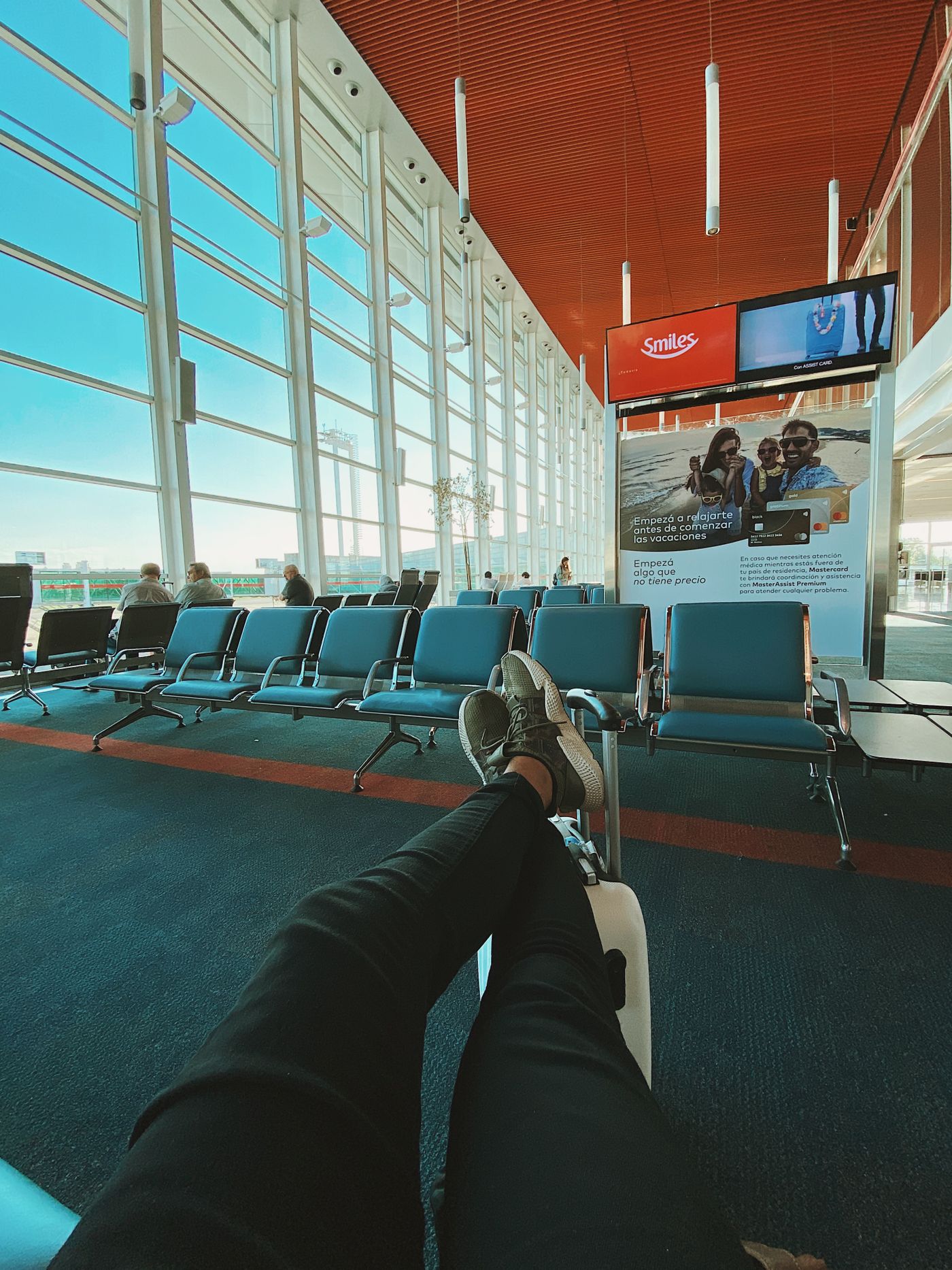 A traveller's legs stretched out while resting in a largely empty airport terminal seating area