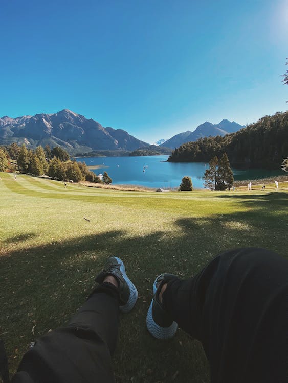 Man lying on lawn near lake in mountainous terrain