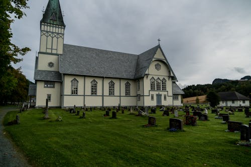 Exterior of old catholic chapel located near stone graveyard under gray sky in countryside in daytime