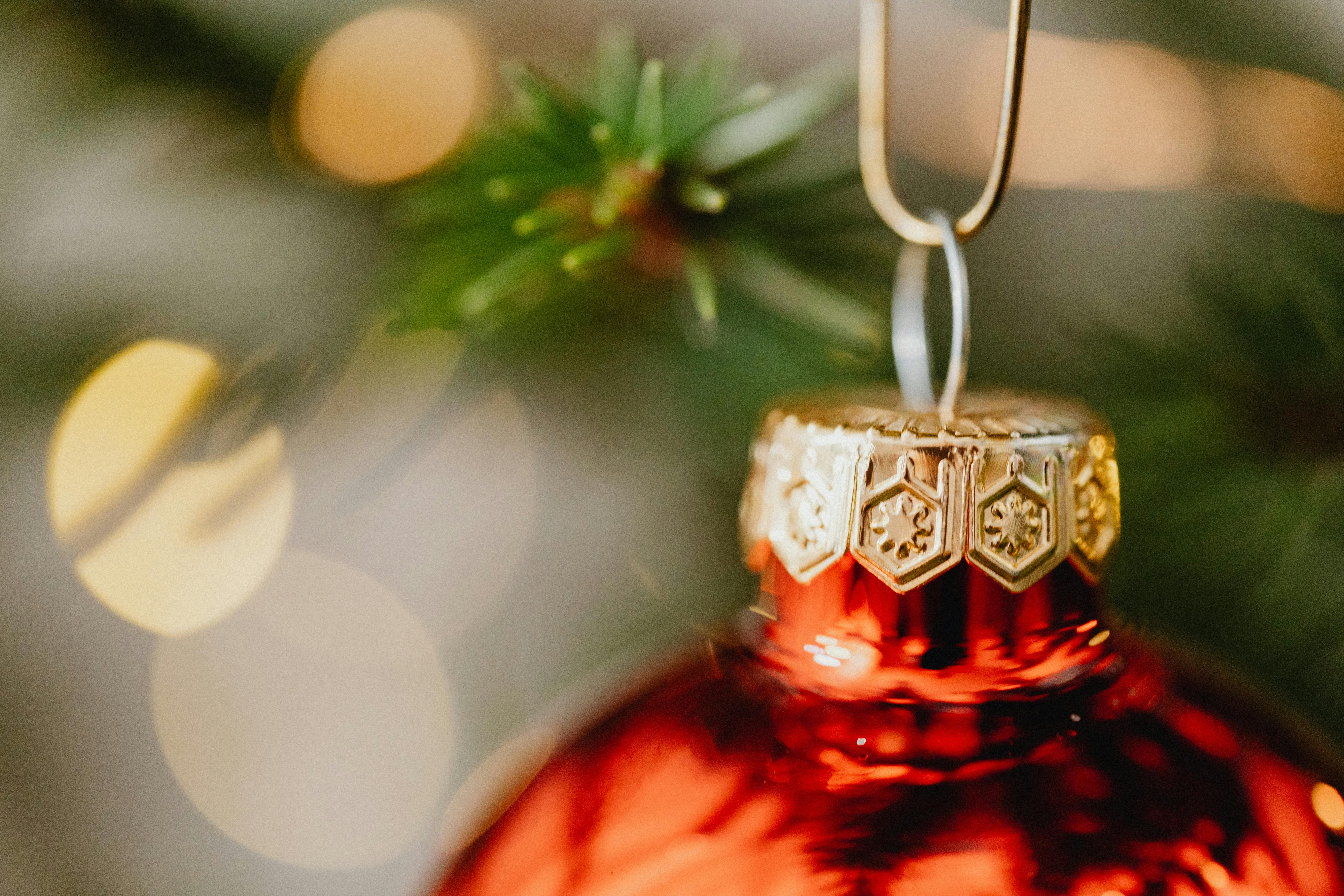 Festive red Christmas bauble hanging on green tree branch with soft bokeh lights.