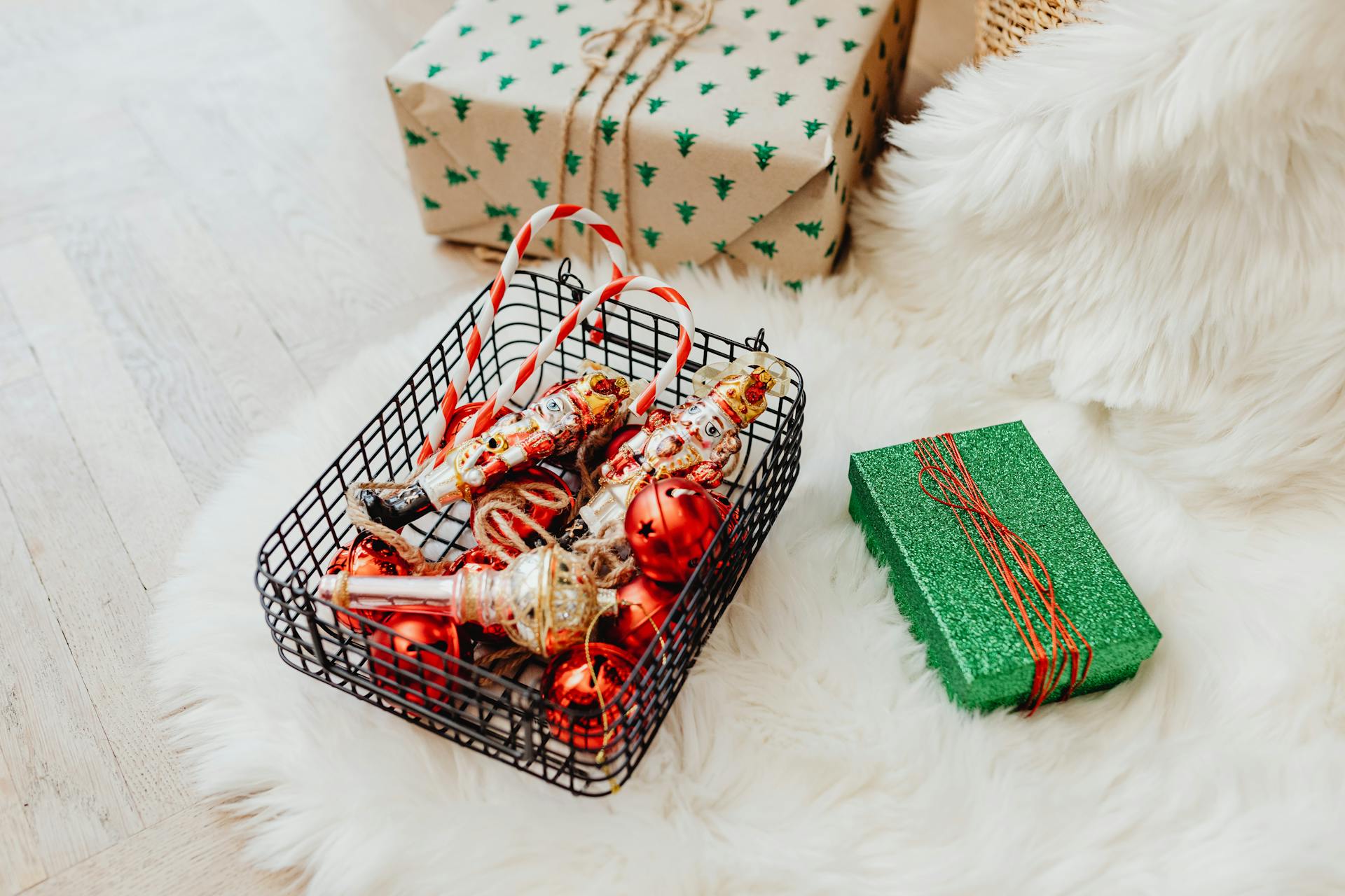 A cozy arrangement of Christmas ornaments in a basket with wrapped gifts on a fluffy rug.