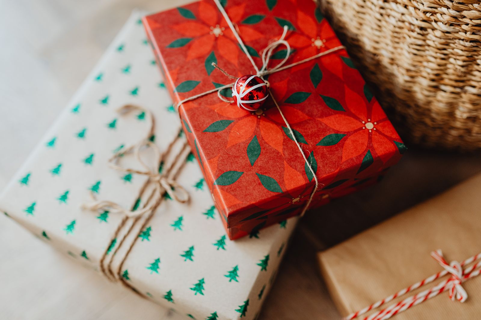 Trois paquets posés sur un sol clair : l'un en papier blanc à sapins verts et l'autre en papier rouge à fleurs, noués de ficelle de jute, le troisième en papier kraft noué d'une ficelle rouge et blanche