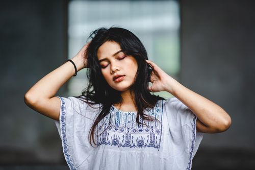 Free Portrait of a serene woman with closed eyes in a white embroidered blouse indoors. Stock Photo