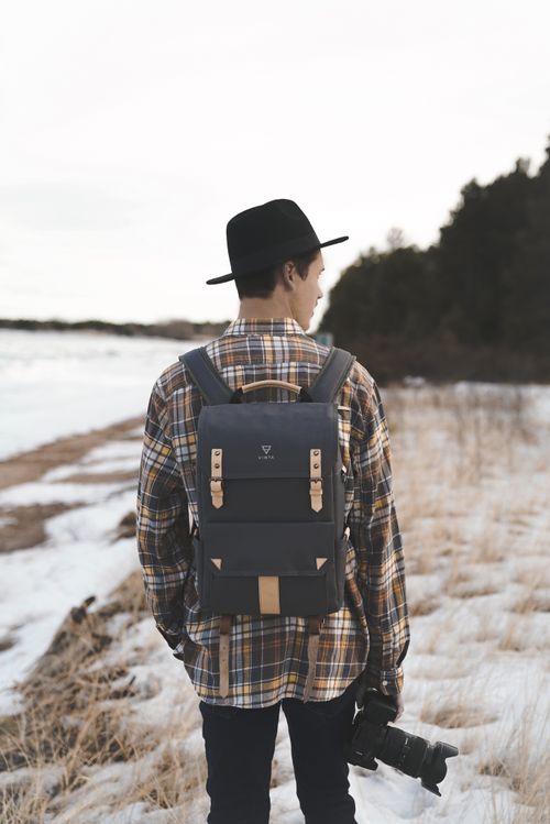 Free Back view of faceless male in warm clothes and hat with backpack looking away on snowy field near winter forest in soft daylight Stock Photo