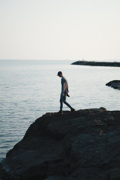 Faceless traveler standing on rocky cliff near sea