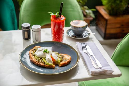 Free Savor a delightful breakfast featuring avocado toast, poached eggs, cappuccino, and a refreshing drink indoors. Stock Photo
