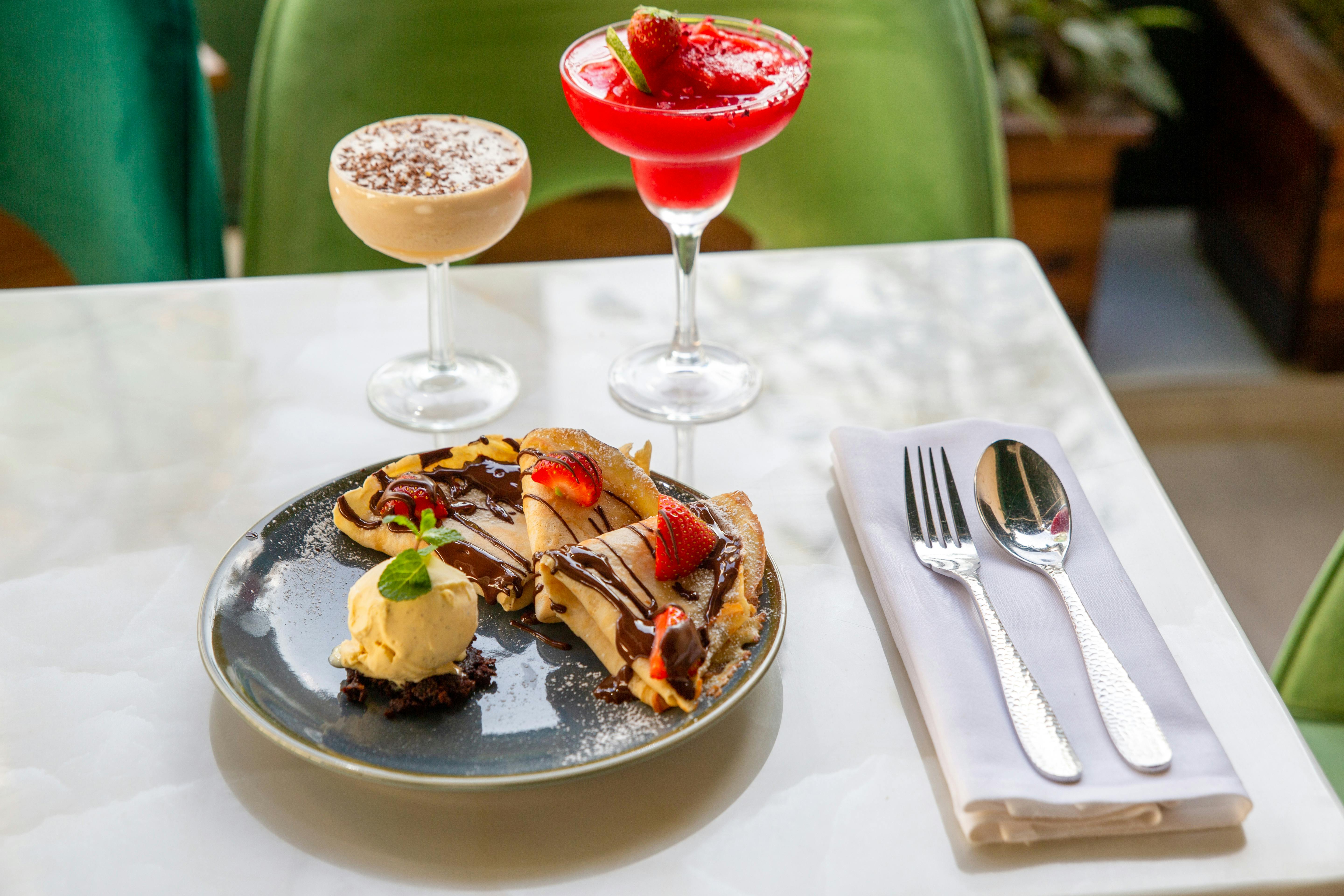 Elegant table setting with crepes, cocktails, and cutlery, perfect for a sweet indulgence.