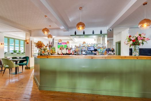 A cozy and stylish bar interior with green counter, wooden flooring, and floral arrangements.