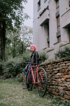 一位粉发时髦女子在城市街区的现代建筑旁骑行